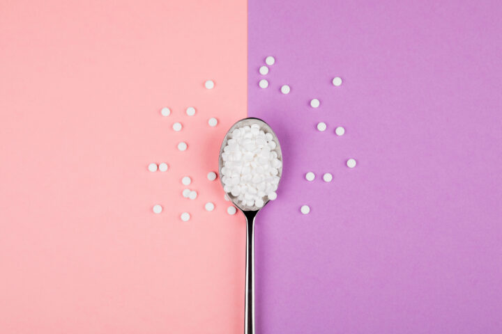 Sugar replacing tablets with a spoon on a pink and purple background
