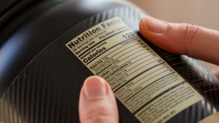 Close up shot of a black jar of whey protein powder with nutrition facts label in person hands.