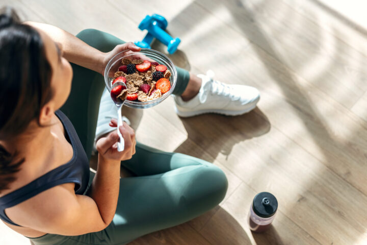 Athletic woman eating a healthy bowl of muesli with fruit sittin
